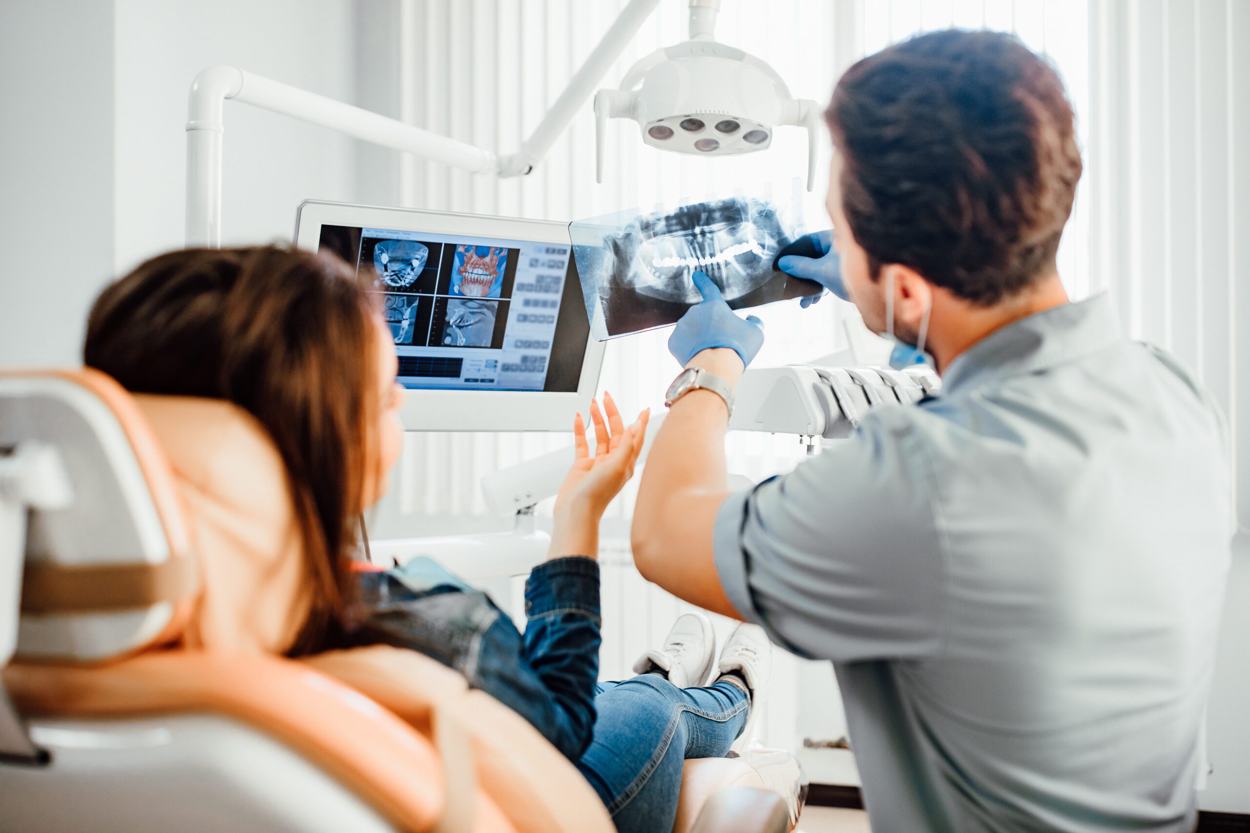 Medicine, dentistry and healthcare concept, male dentist showing teeth x-ray to female patient at dental clinic office.